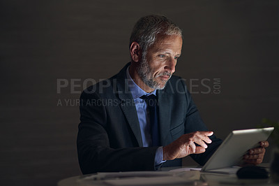 Buy stock photo Shot of a mature businessman using a digital tablet while working late in an office