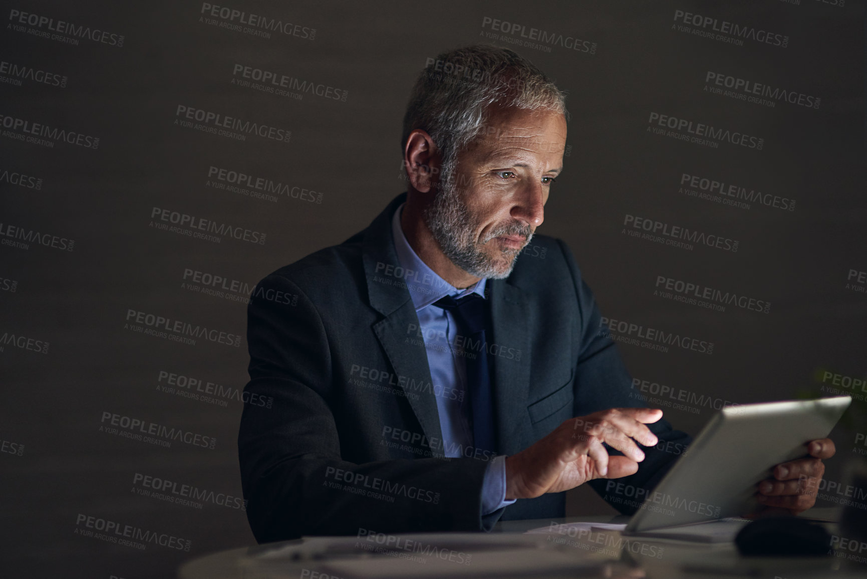 Buy stock photo Shot of a mature businessman using a digital tablet while working late in an office