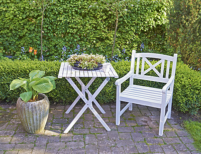 Buy stock photo White wooden chair and table in a green garden with blossoming plants and copyspace. Tranquil landscape to relax and enjoy a cosy picnic in summertime. Outdoor patio in a quiet and secluded courtyard