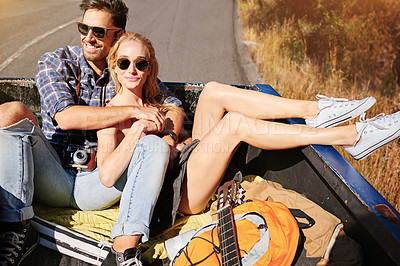 Buy stock photo Shot of a young couple relaxing on the back of a pickup truck while on a road trip