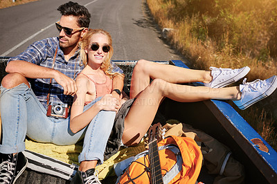 Buy stock photo Shot of a young couple relaxing on the back of a pickup truck while on a road trip