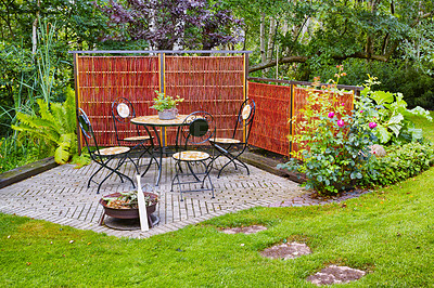 Buy stock photo Chairs and a table in a beautiful garden or botanical area during spring or summer. Outdoor furniture in the backyard with lush green plants and flowers. A peaceful, serene, and private area at home