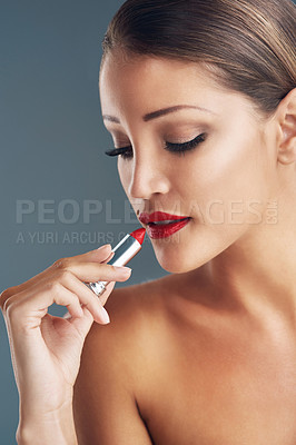 Buy stock photo Studio shot of a beautiful young woman putting on red lipstick against a grey background