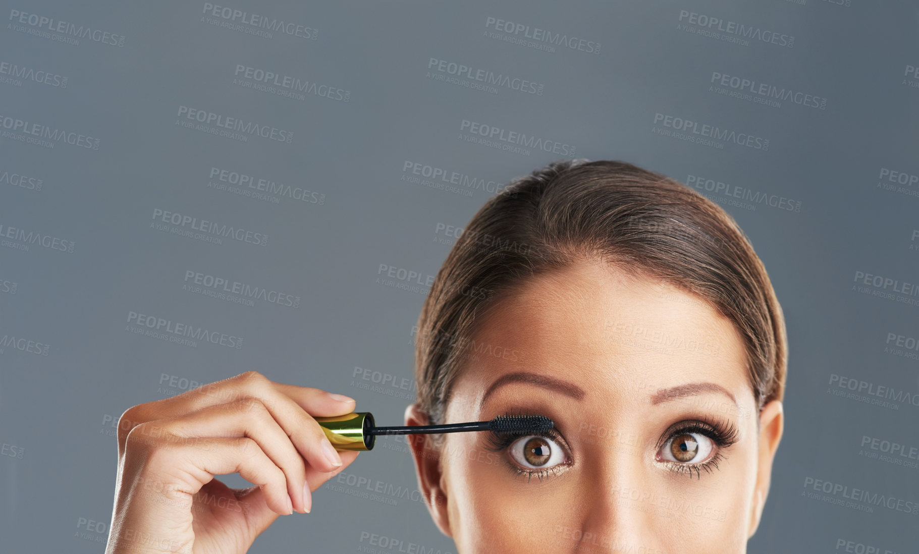 Buy stock photo Studio portrait of a beautiful young woman putting on mascara against a grey background