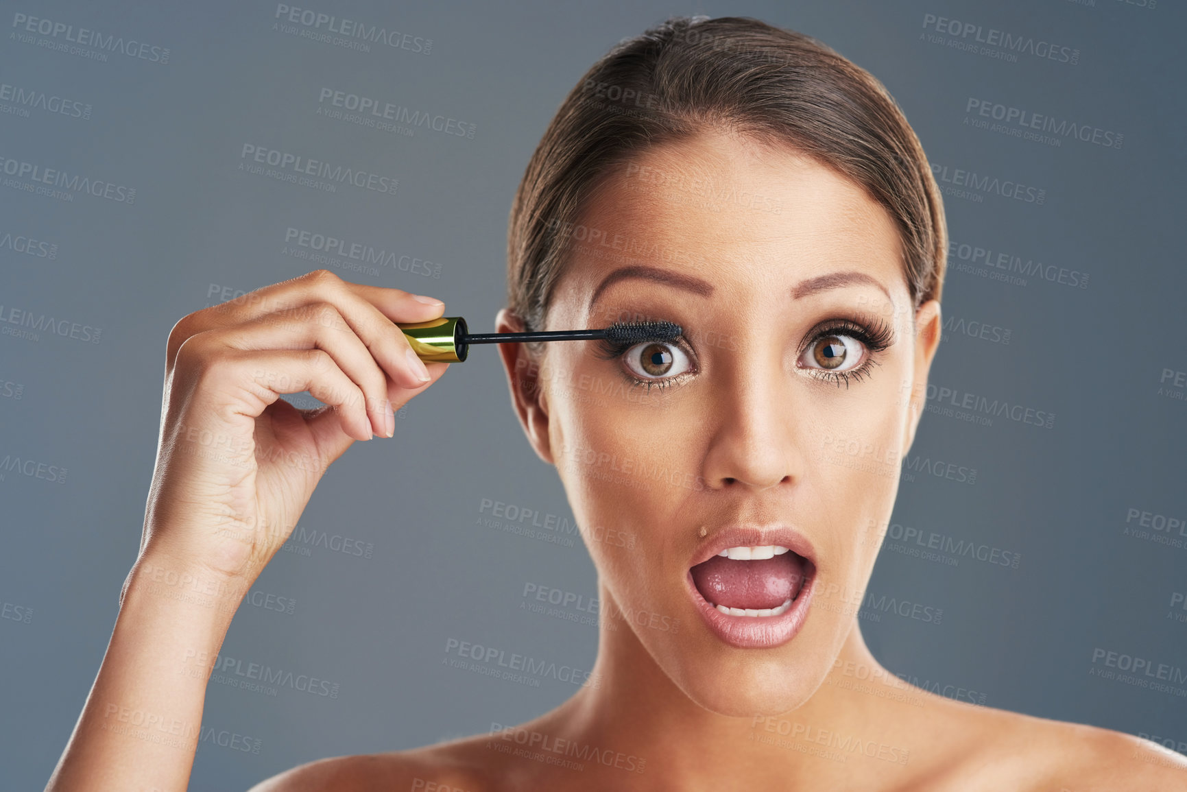 Buy stock photo Studio portrait of a beautiful young woman putting on mascara against a grey background