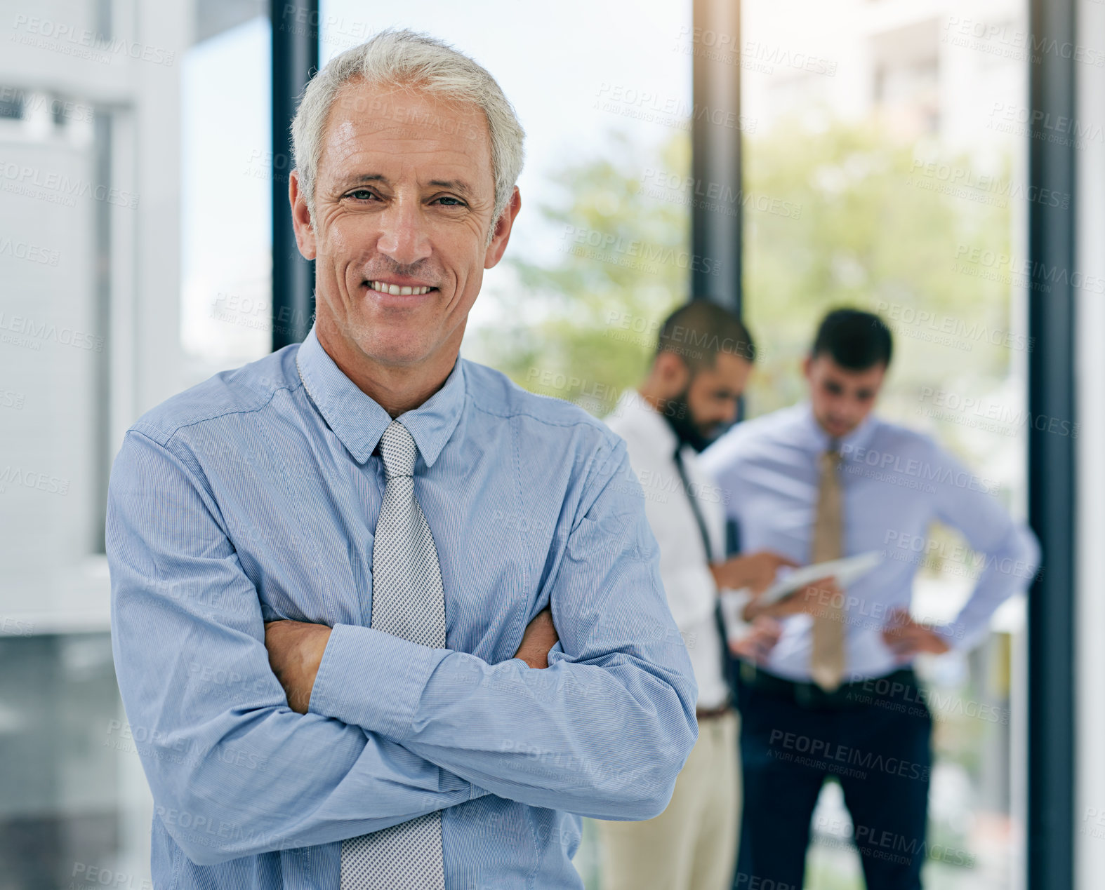 Buy stock photo Portrait of a mature businessman standing in an office with colleagues in the background