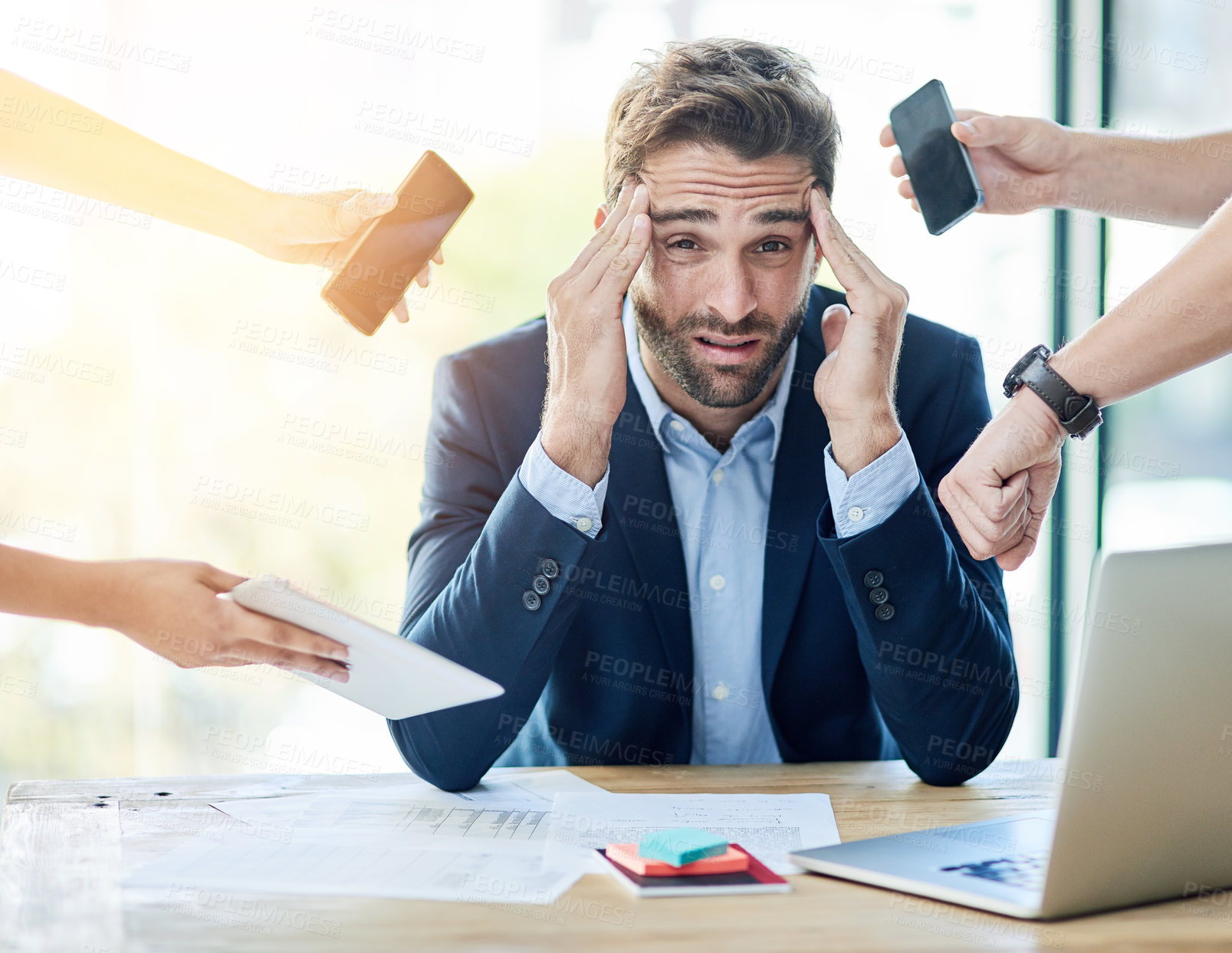 Buy stock photo Portrait of a young businessman sitting at a desk surrounded by hands reaching in holding items