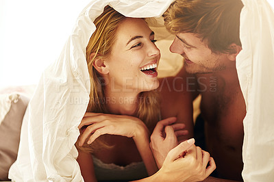 Buy stock photo Shot of a young couple sharing an intimate moment under the covers in bed