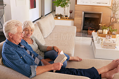 Buy stock photo Shot of a relaxed senior couple reading a book together on the sofa at home