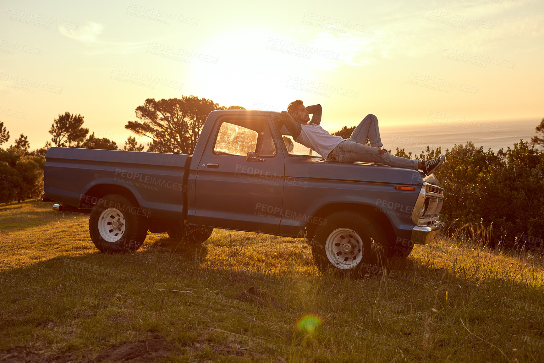 Buy stock photo Shot of a young man lying on the roof of his truck on a roadtrip