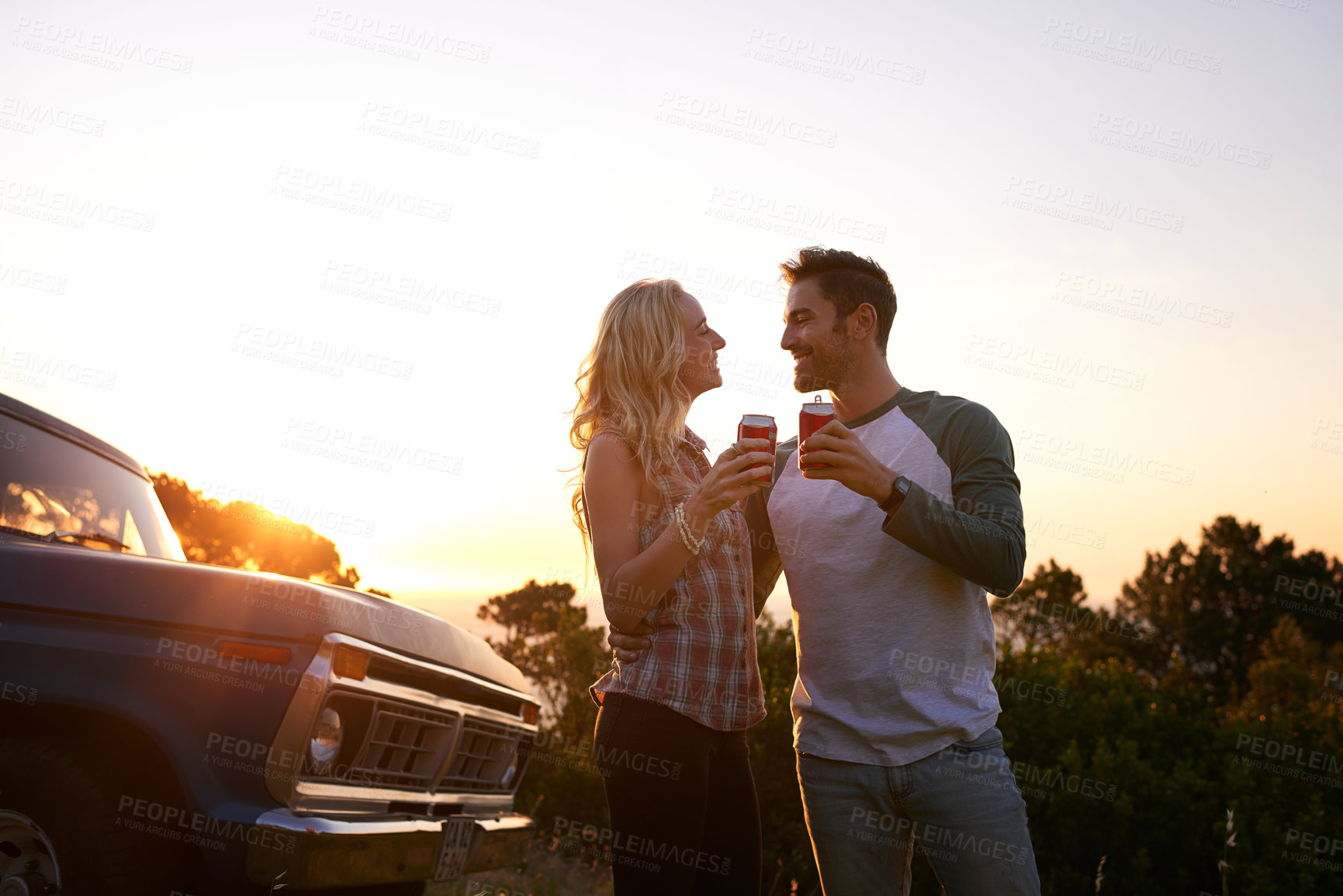 Buy stock photo Cheers, nature and couple by car for travel by sunset on vacation, weekend or holiday. Happy, beer and young man and woman outdoor in field by vehicle for road trip getaway together in evening.