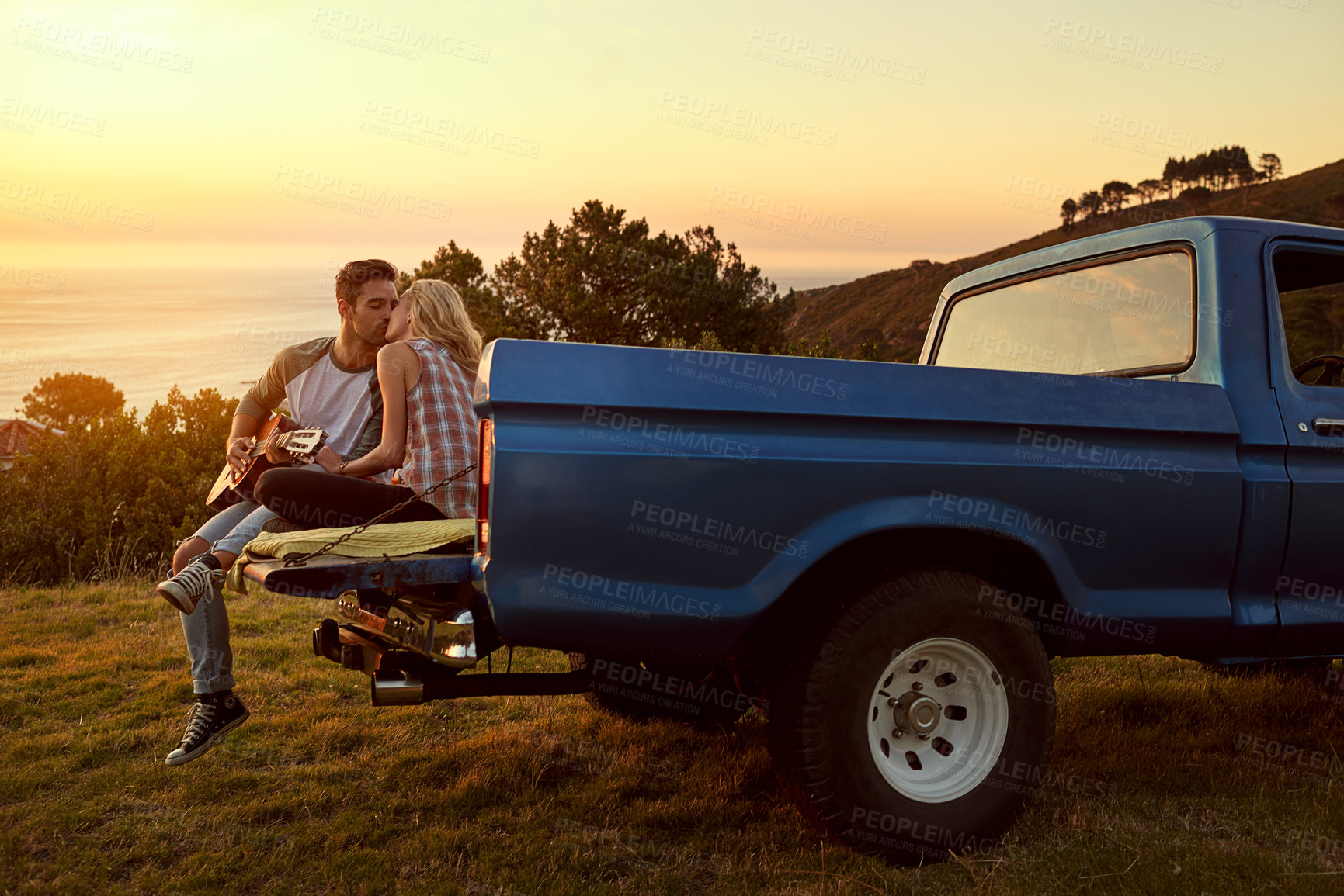 Buy stock photo Shot of a young man playing guitar for his girlfriend on a roadtrip