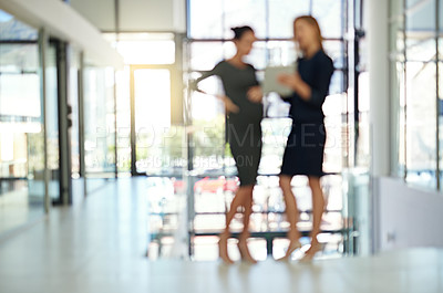 Buy stock photo Blurred shot of two businesswomen talking together over a digital tablet in a modern office