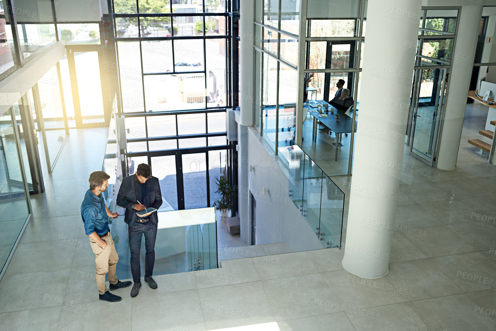 Buy stock photo Shot of two colleagues talking together over a digital tablet while standing in a modern office