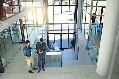 Buy stock photo Shot of two colleagues talking together over a digital tablet while standing in a modern office