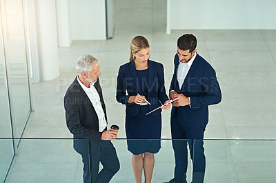 Buy stock photo Shot of three colleagues talking together over a digital tablet while standing in a modern office
