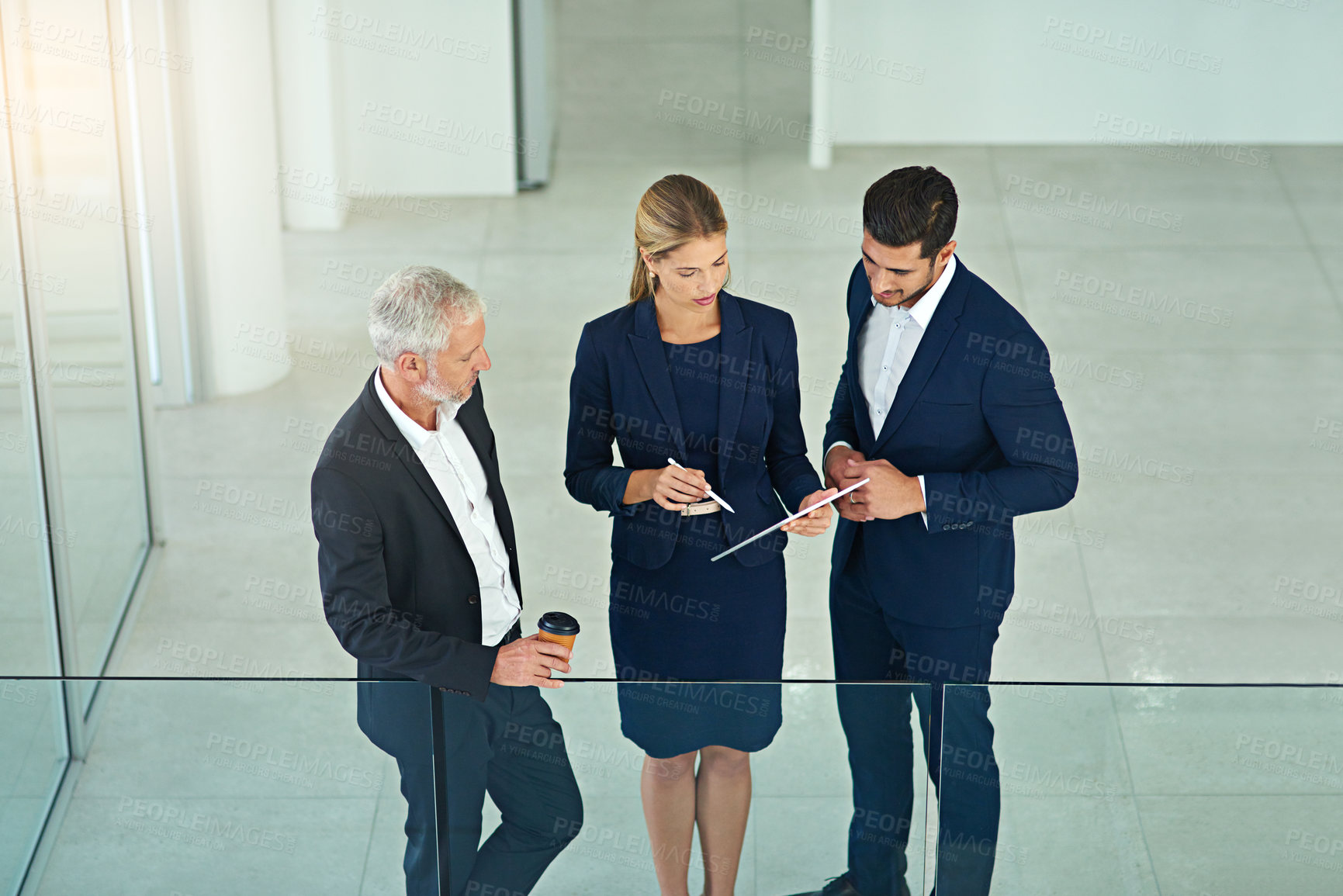 Buy stock photo Shot of three colleagues talking together over a digital tablet while standing in a modern office