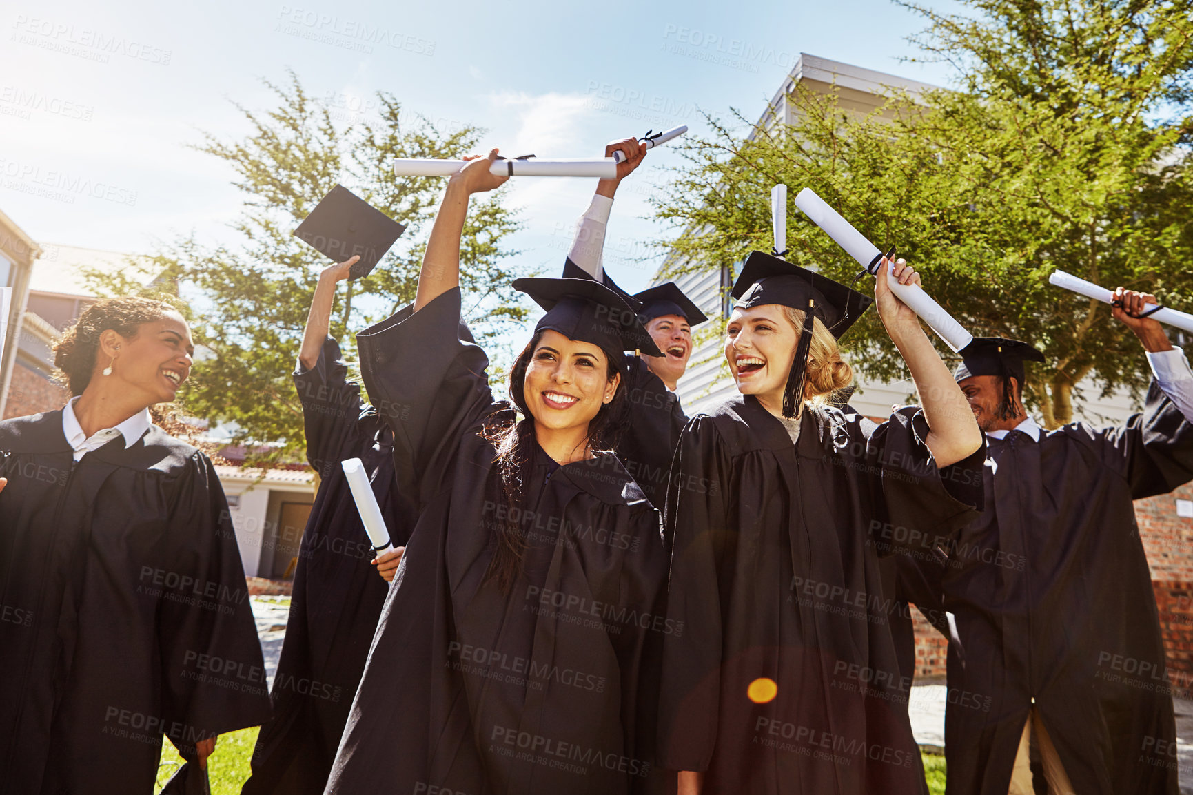Buy stock photo Shot of a group of smiling university students cheering outside on graduation day