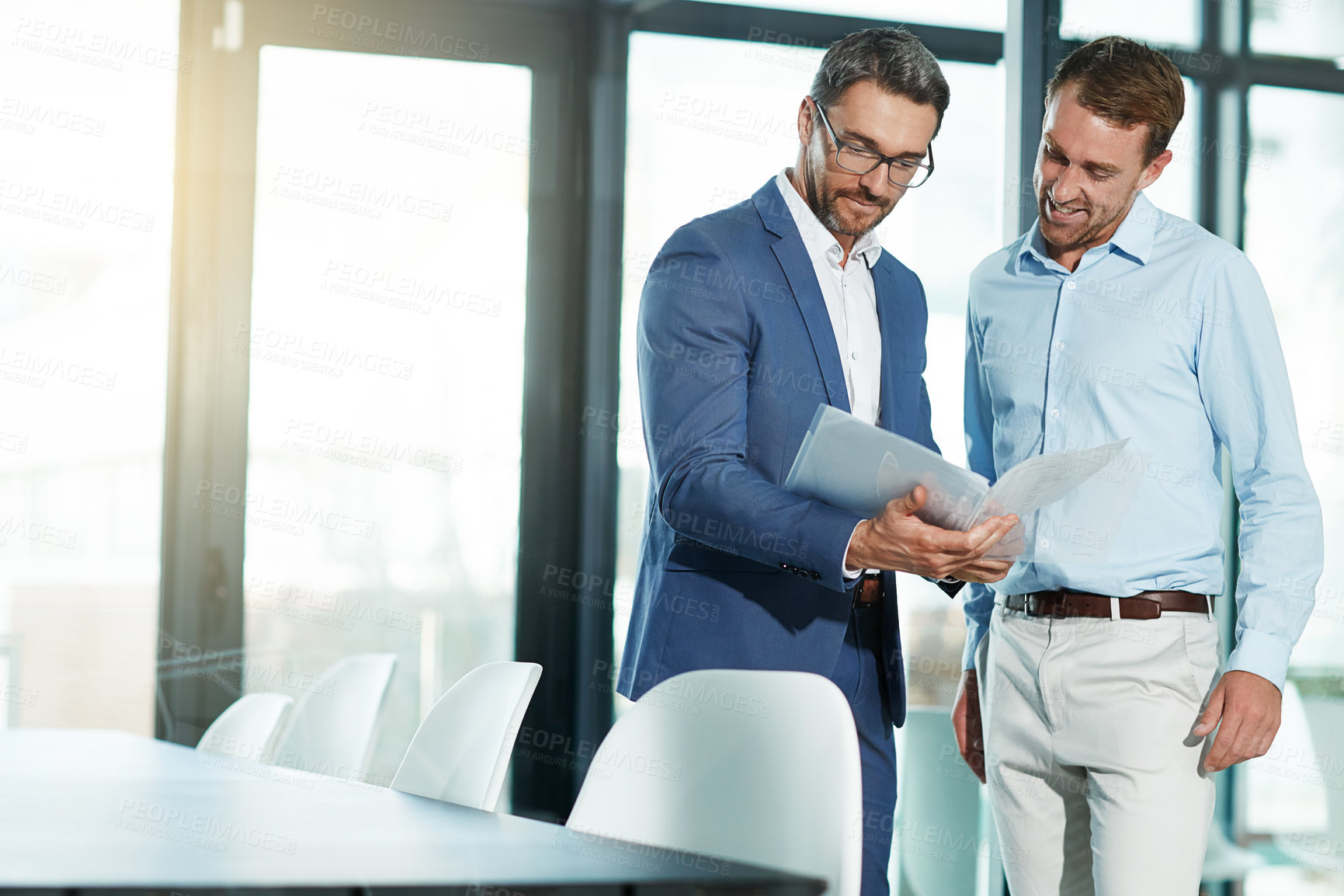 Buy stock photo Shot of two businessmen talking over some paperwork in an office