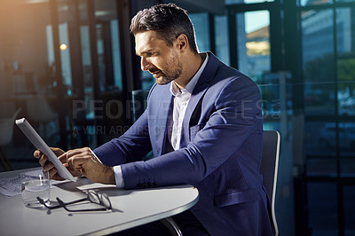 Buy stock photo Shot of a businessman using a digital tablet while woking late at the office