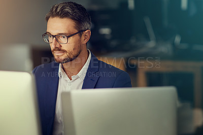 Buy stock photo Shot of a businessman using a computer while woking late at the office