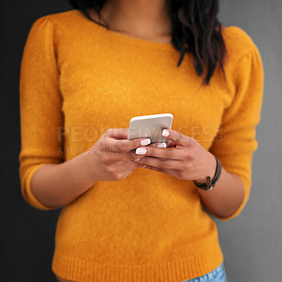 Buy stock photo Cropped studio shot of a young woman using her phone against a gray background