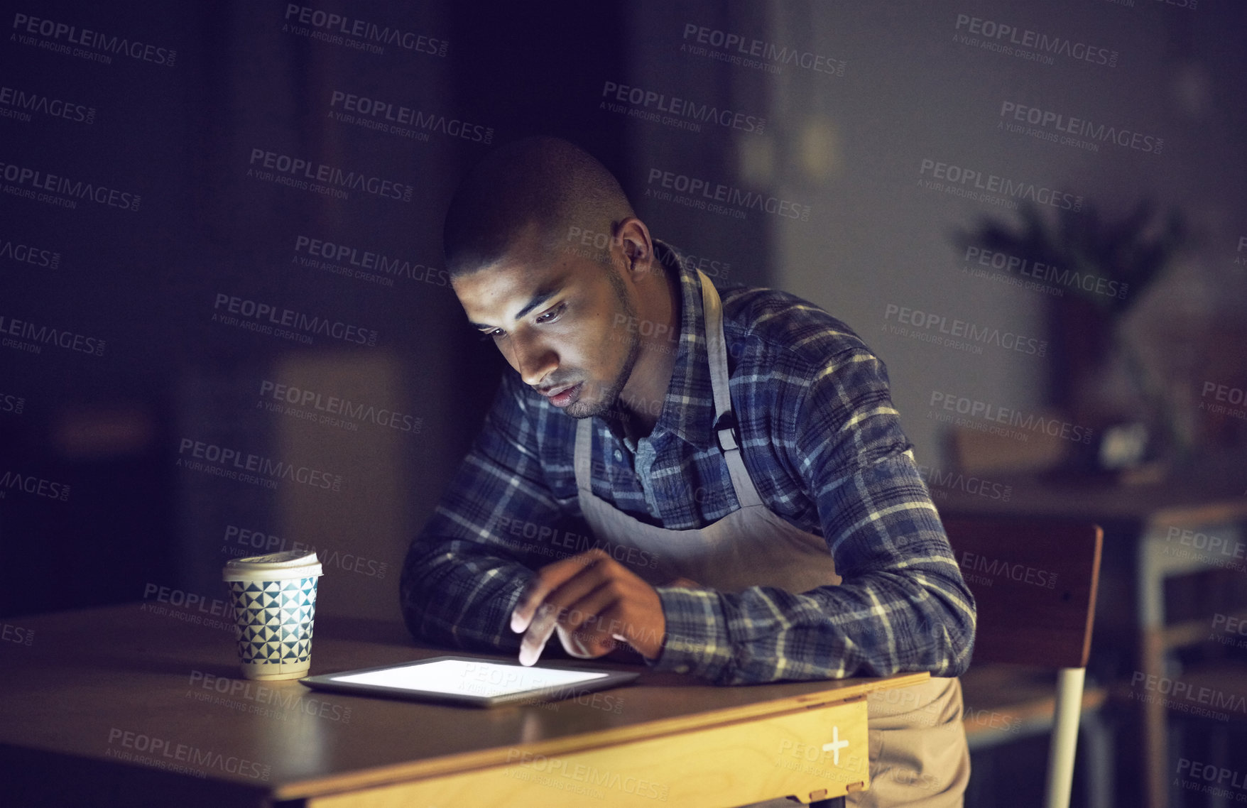 Buy stock photo Shot of a young man working late on a digital tablet in his coffee shop