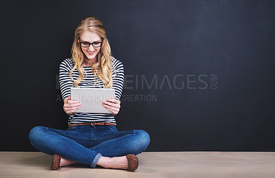 Buy stock photo Studio shot of a young woman using a digital tablet against a dark background