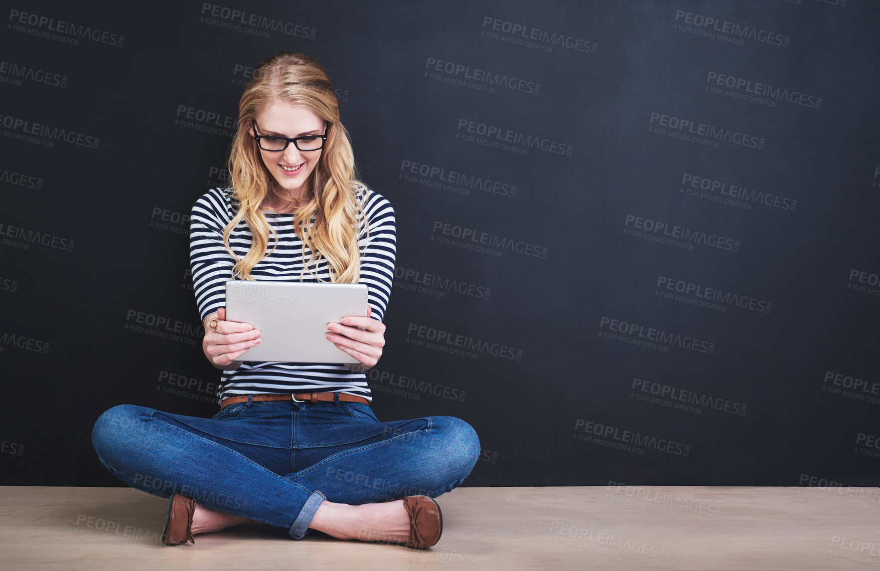 Buy stock photo Studio shot of a young woman using a digital tablet against a dark background