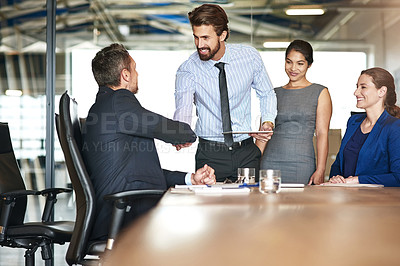 Buy stock photo Shot of two businesspeople shaking hands while in a meeting with colleagues in a boardroom