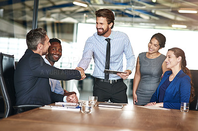 Buy stock photo Shot of two colleagues shaking hands while in a meeting with colleagues in a boardroom