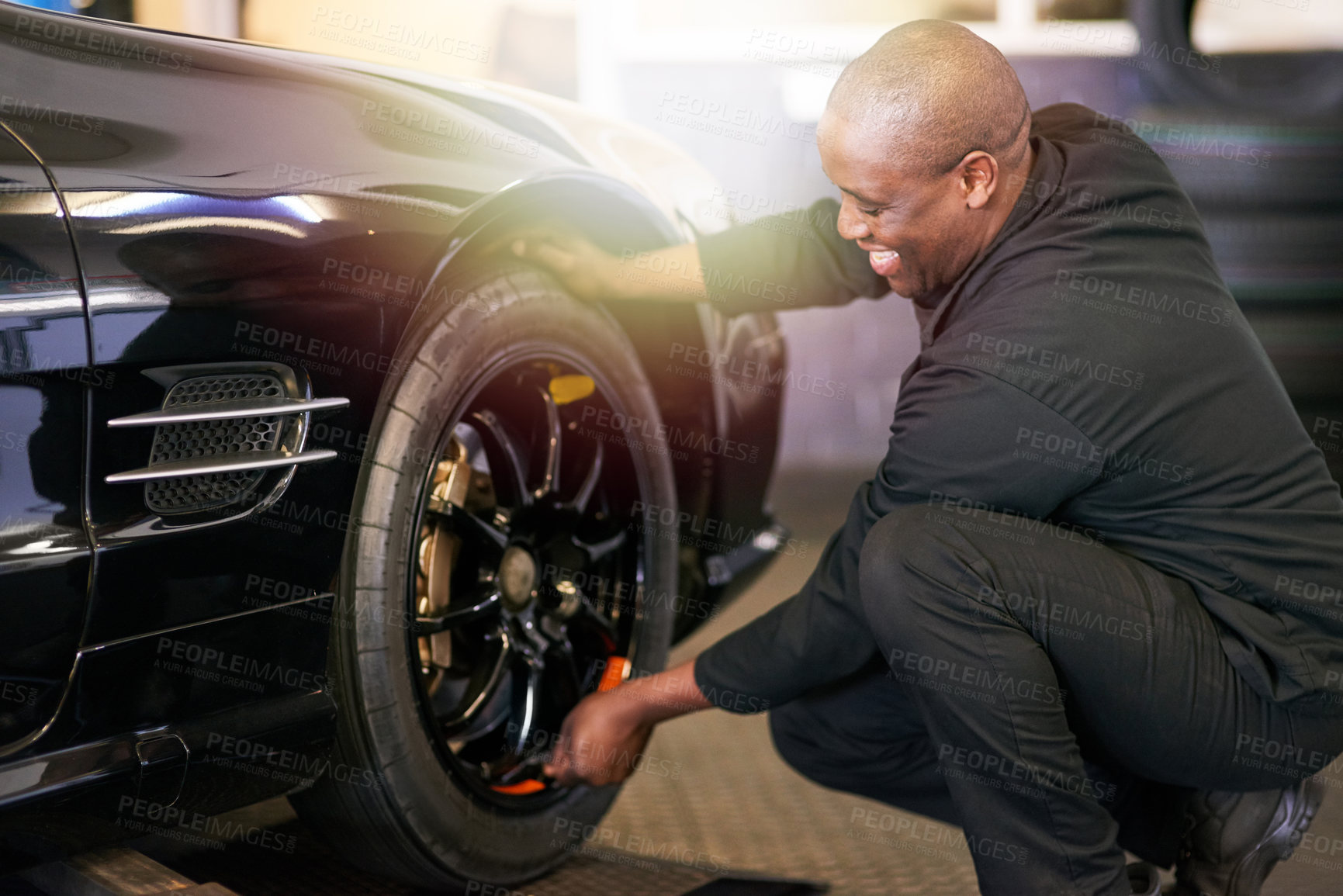 Buy stock photo Tyre, black man and wheel in garage for repairs, rubber and fixing or replace fitting on car at shop. Mechanic, happy and service or safety check inspection, motor and alignment of vehicle to change