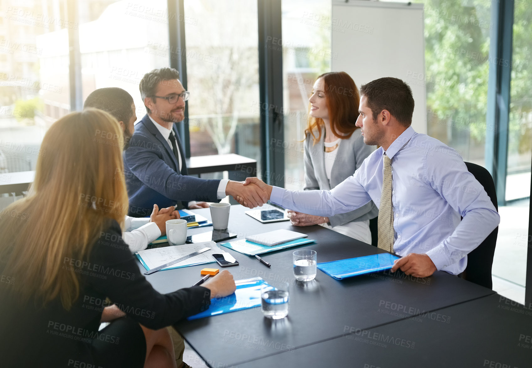 Buy stock photo Cropped shot of two businessmen shaking hands while sitting in a meeting