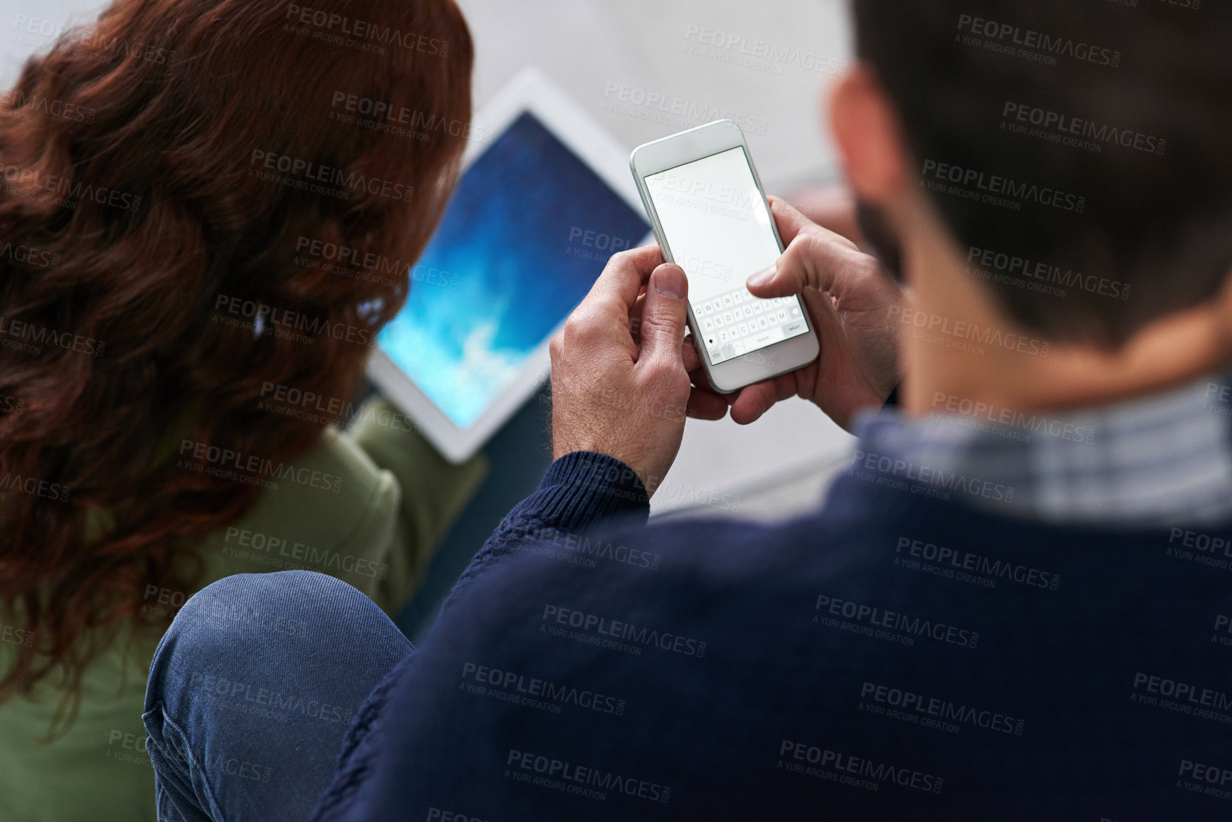 Buy stock photo Shot of two business people using a cellphone and a tablet in an office