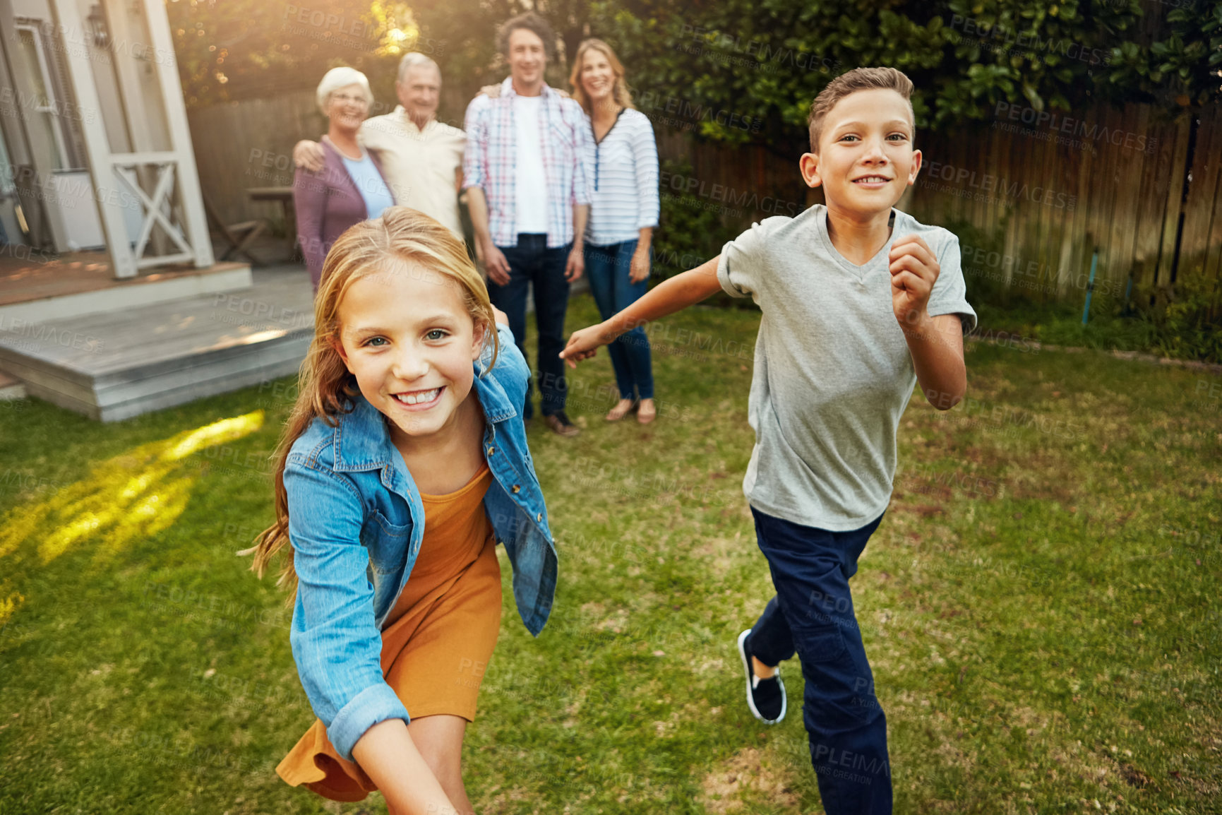 Buy stock photo Shot of a young brother and sister playing togther in the yard with their family in the background
