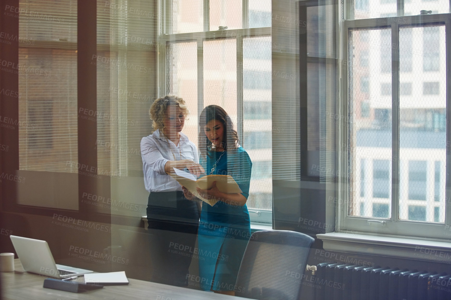 Buy stock photo Shot of two businesswomen going over paperwork together in an office