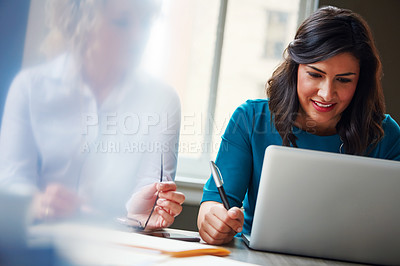 Buy stock photo Shot of two businesswomen using a laptop together in an office