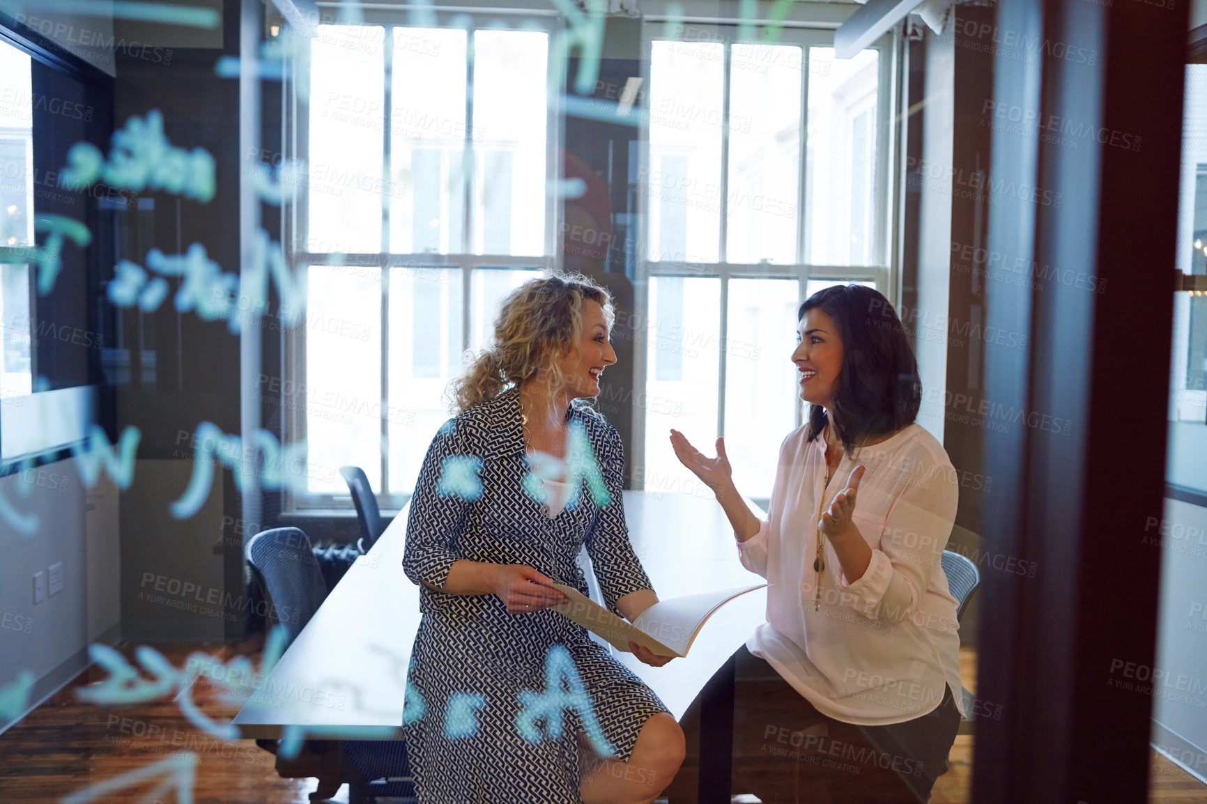 Buy stock photo Shot of two businesswoman brainstorming on a glass wall in an office