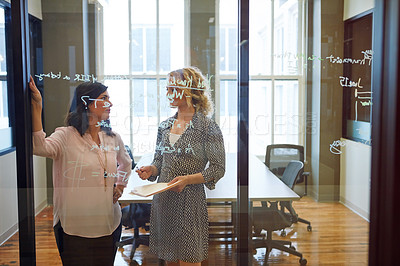 Buy stock photo Shot of two businesswoman brainstorming on a glass wall in an office