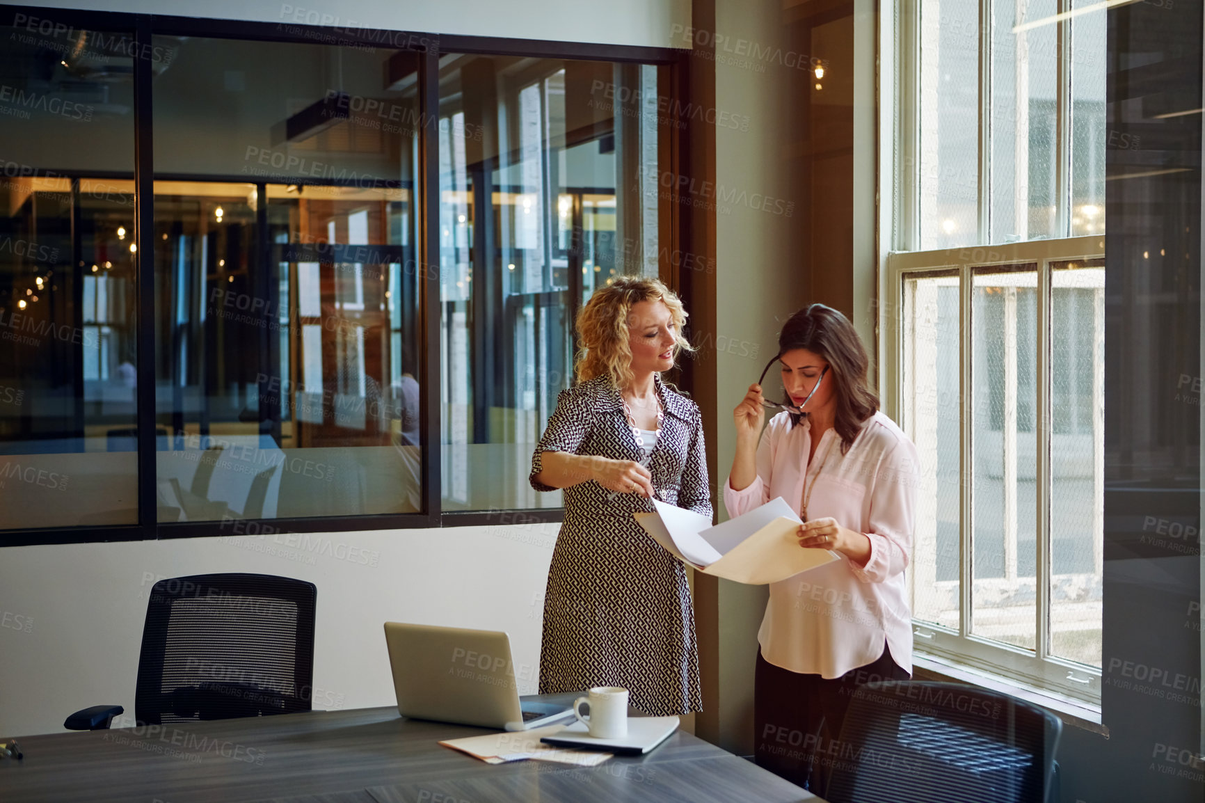 Buy stock photo Shot of two businesswomen talking together over paperwork in an office