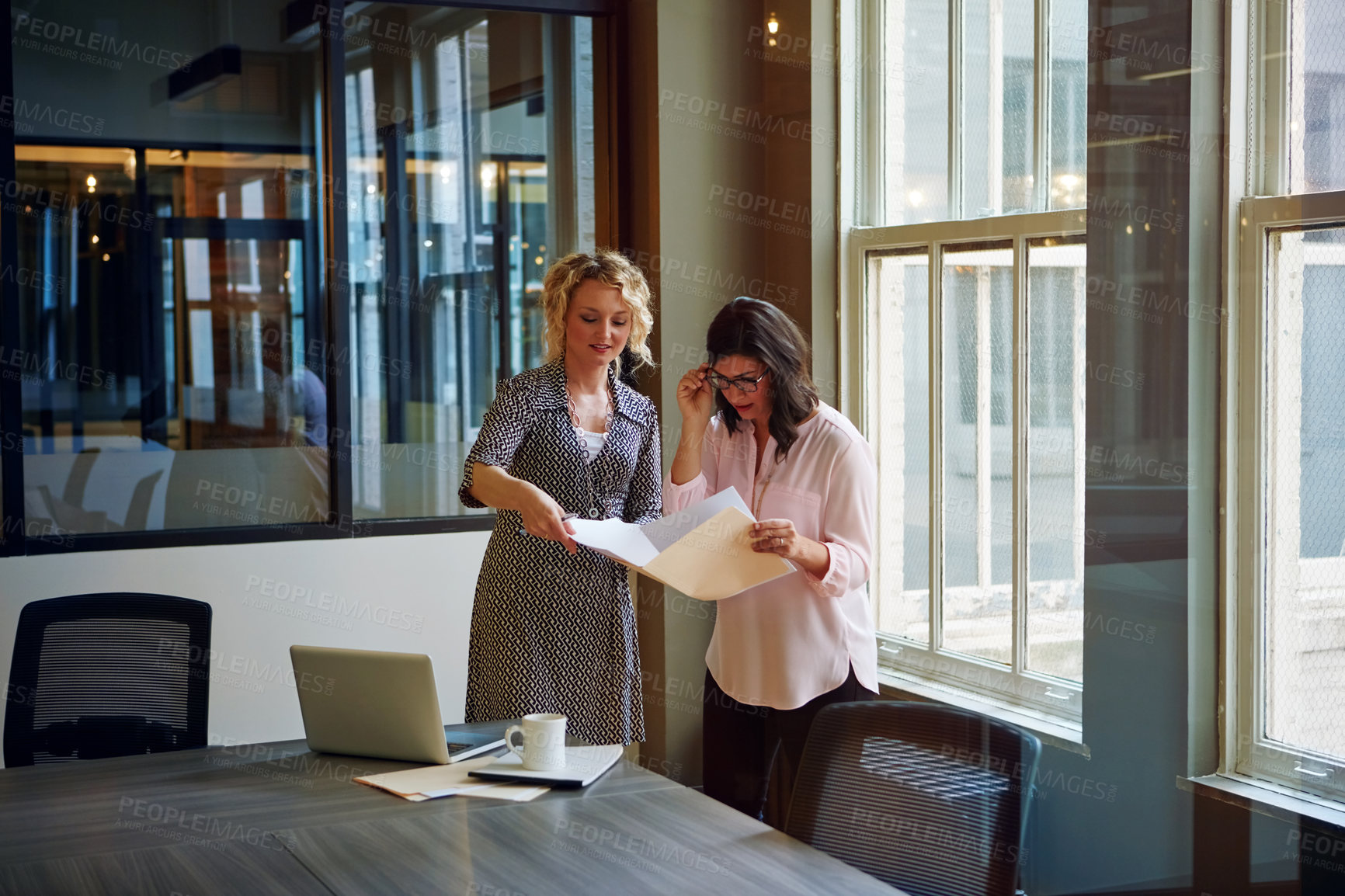 Buy stock photo Shot of two businesswomen talking together over paperwork in an office