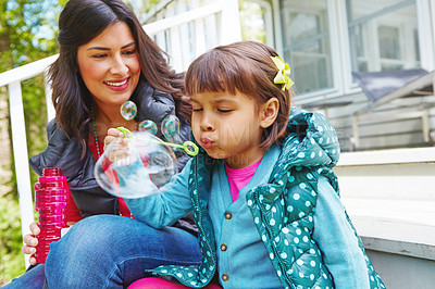 Buy stock photo Cropped shot of a mother watching her daughter blow bubbles outside