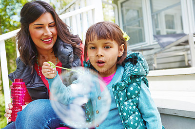Buy stock photo Cropped shot of a mother watching her daughter blow bubbles outside