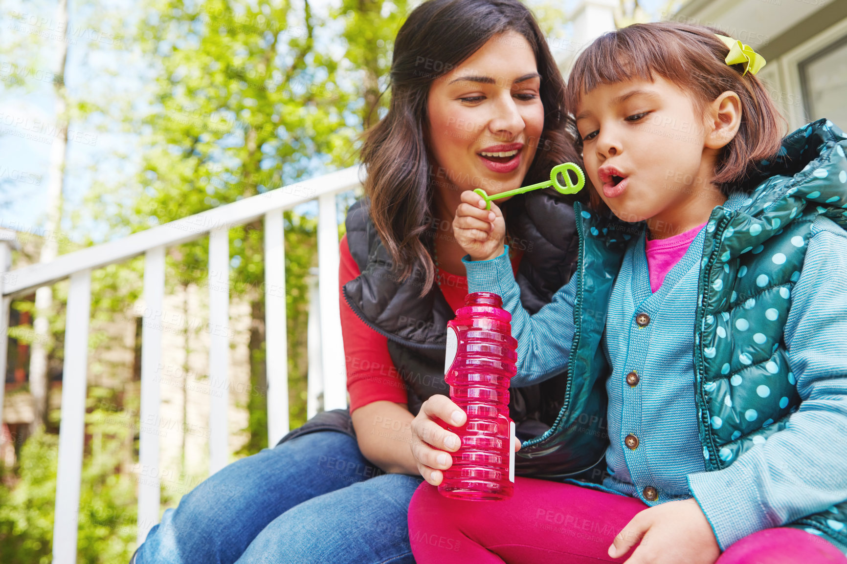 Buy stock photo Cropped shot of a mother watching her daughter blow bubbles outside