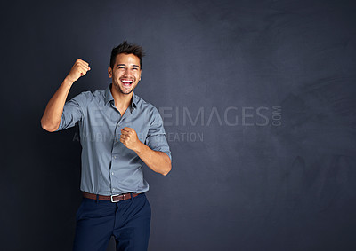 Buy stock photo Studio shot of a young businessman standing with his fists raised in celebration against a dark background