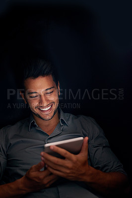 Buy stock photo Business man, tablet and night with smile for meme, social media app or comic video on web, internet or blog. Young businessman, digital touchscreen and reading in dark workplace with funny article