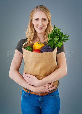 Buy stock photo Cropped studio shot of a young woman holding a paper bag full of vegetables