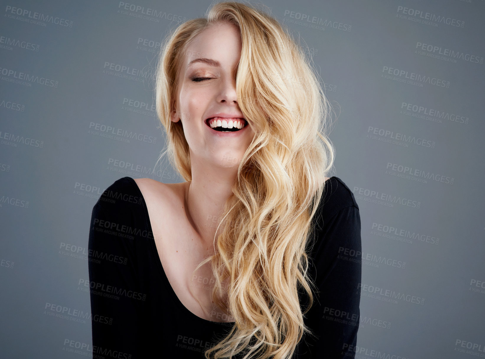 Buy stock photo Studio portrait of an attractive young woman with beautiful long blonde hair laughing against a gray background
