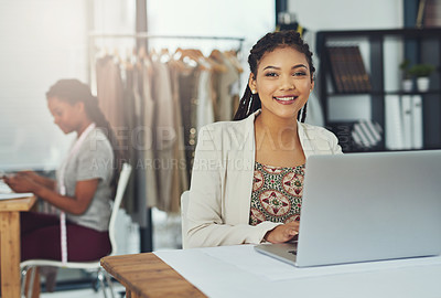 Buy stock photo Shot of a fashion designer working on her laptop with her colleague blurred out