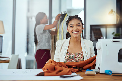Buy stock photo Portrait of a young fashion designer sewing garments while a colleague works on a mannequin in the background